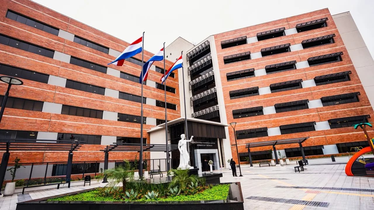 Fachada de ladrillo visto del nuevo edificio judicial en Fernando de la Mora con banderas paraguayas en el patio.