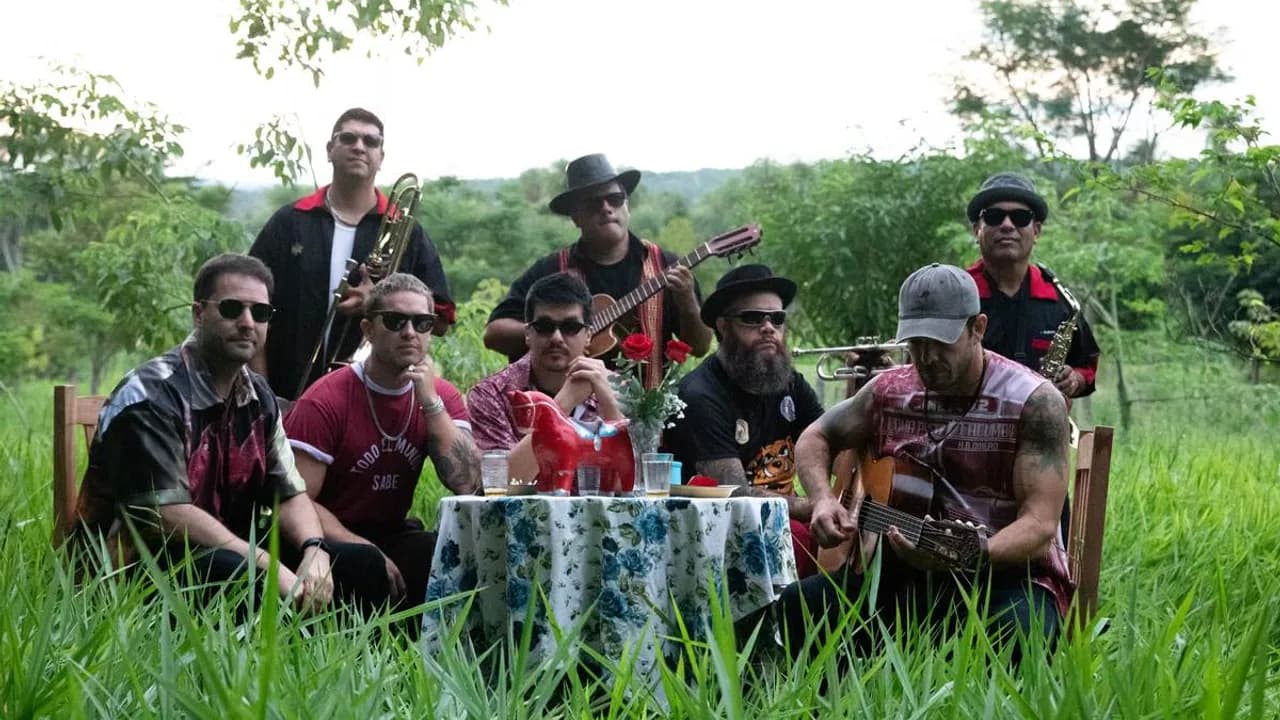 Integrantes de una banda sentados al aire libre alrededor de una mesa decorada con flores e instrumentos.
