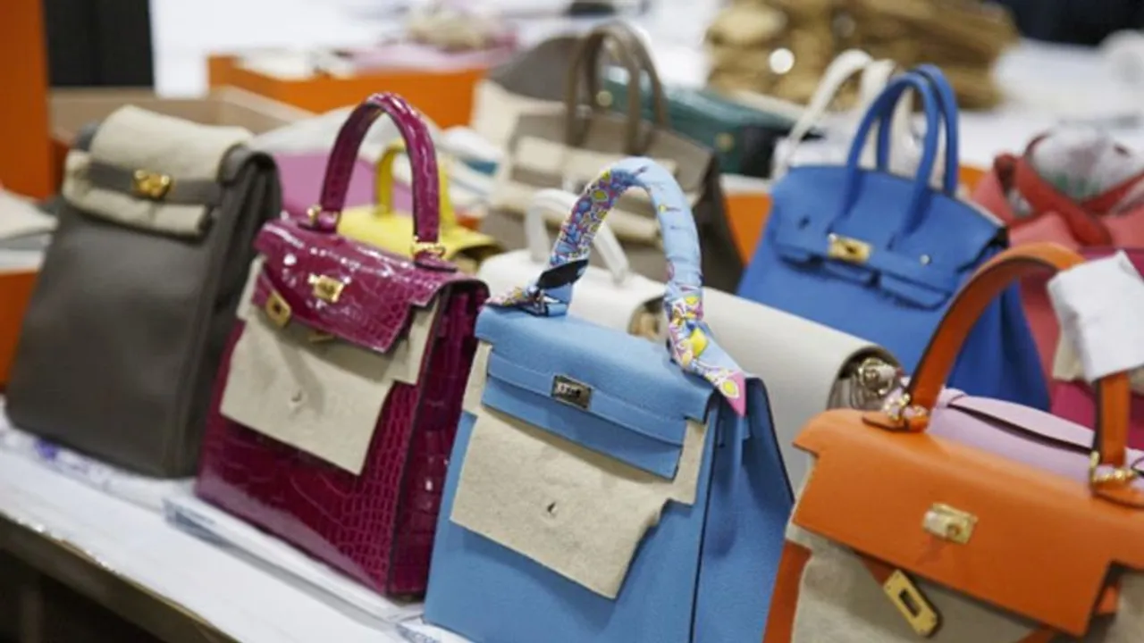 Varios bolsos de mano de lujo en colores azul, fucsia, beige y naranja ordenados sobre una mesa de exhibición.