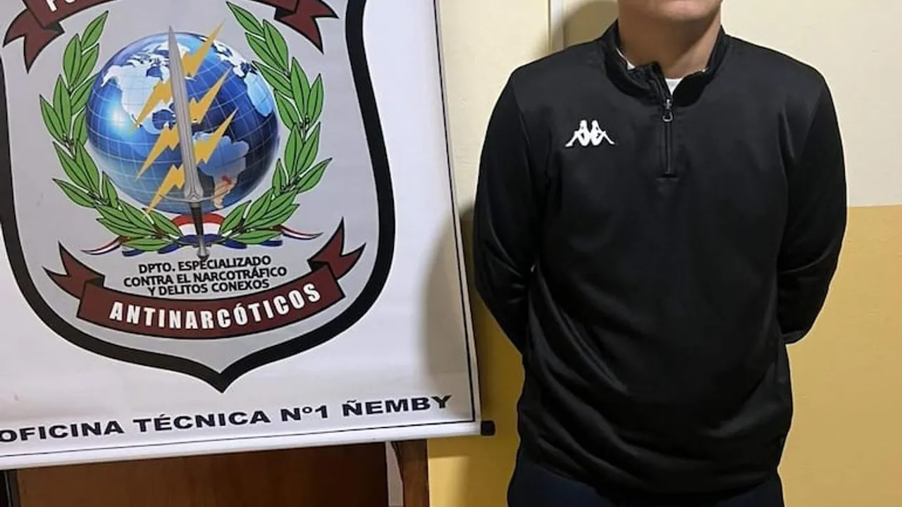 Hombre detenido parado junto a un cartel del Departamento Antinarcóticos de la Policía Nacional.