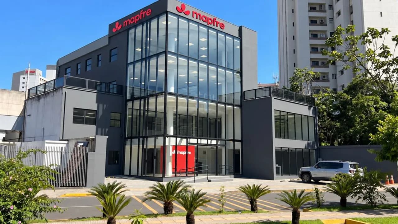 Edificio moderno de tres niveles con fachada vidriada y carteles de Mapfre sobre una calle con palmeras.