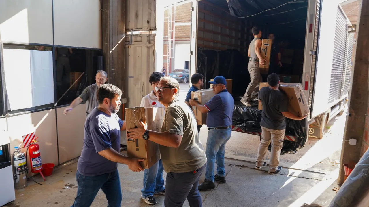 Trabajadores cargan cajas con equipos tecnológicos en la parte trasera de un camión de gran porte.