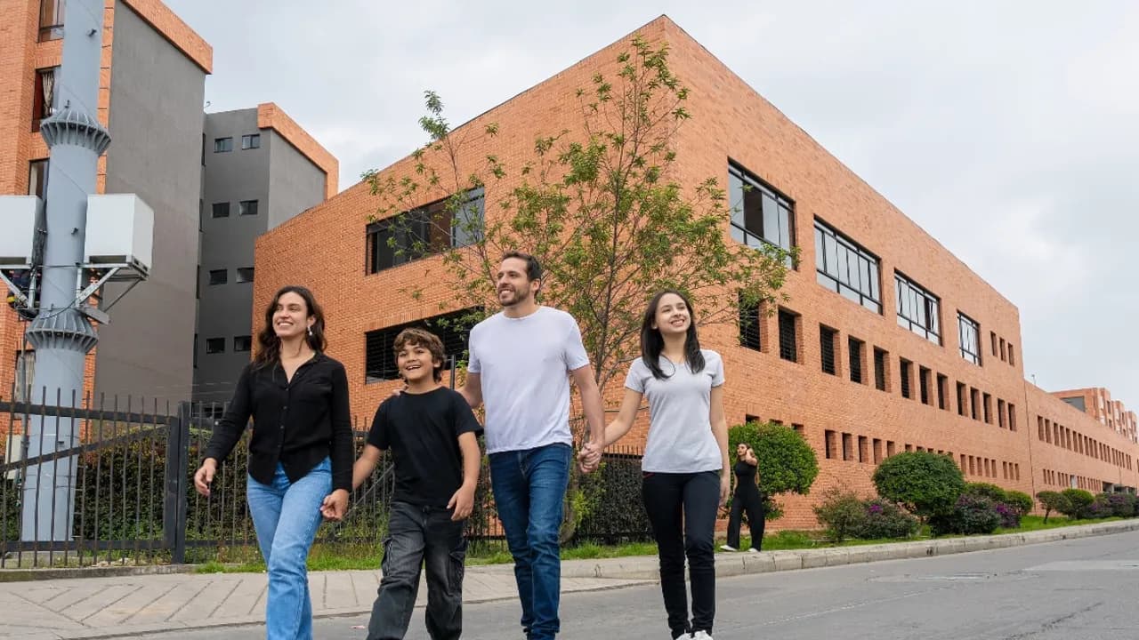 Familia de cuatro personas caminando tomada de la mano sobre una calle frente a un edificio de ladrillos.