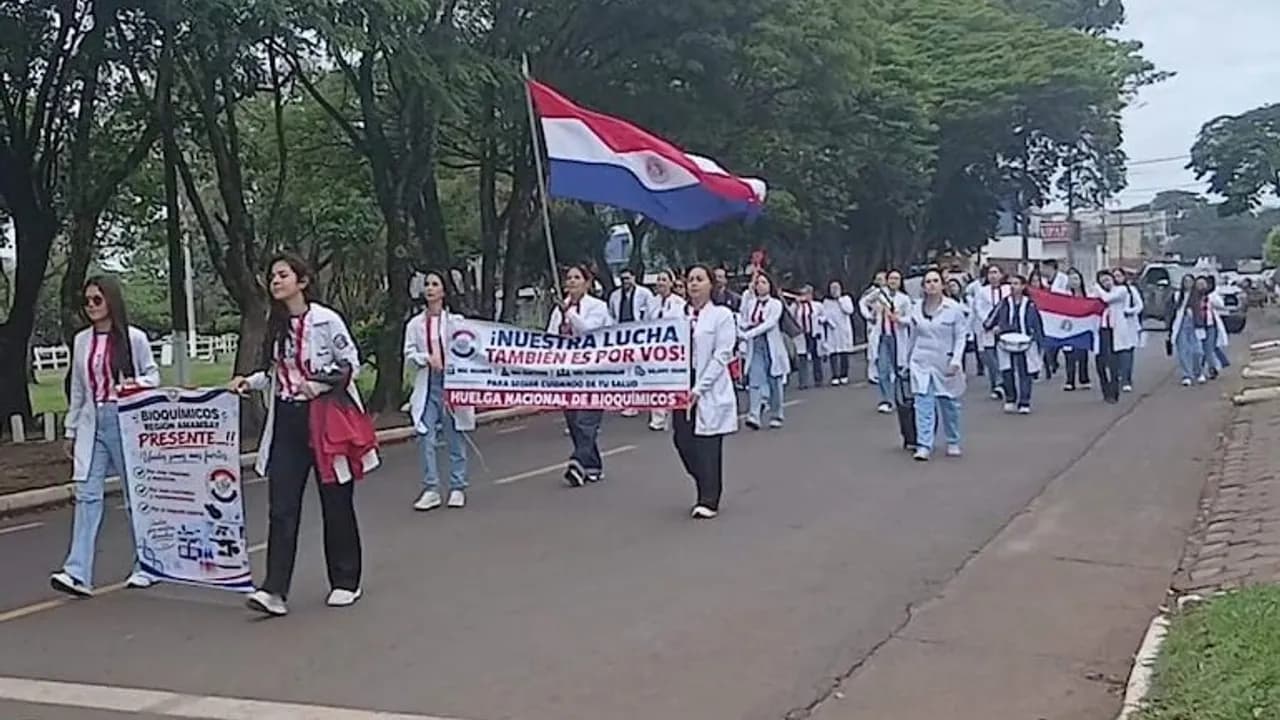 Profesionales de blanco marchan por una calle portando carteles y la bandera paraguaya durante una protesta gremial.