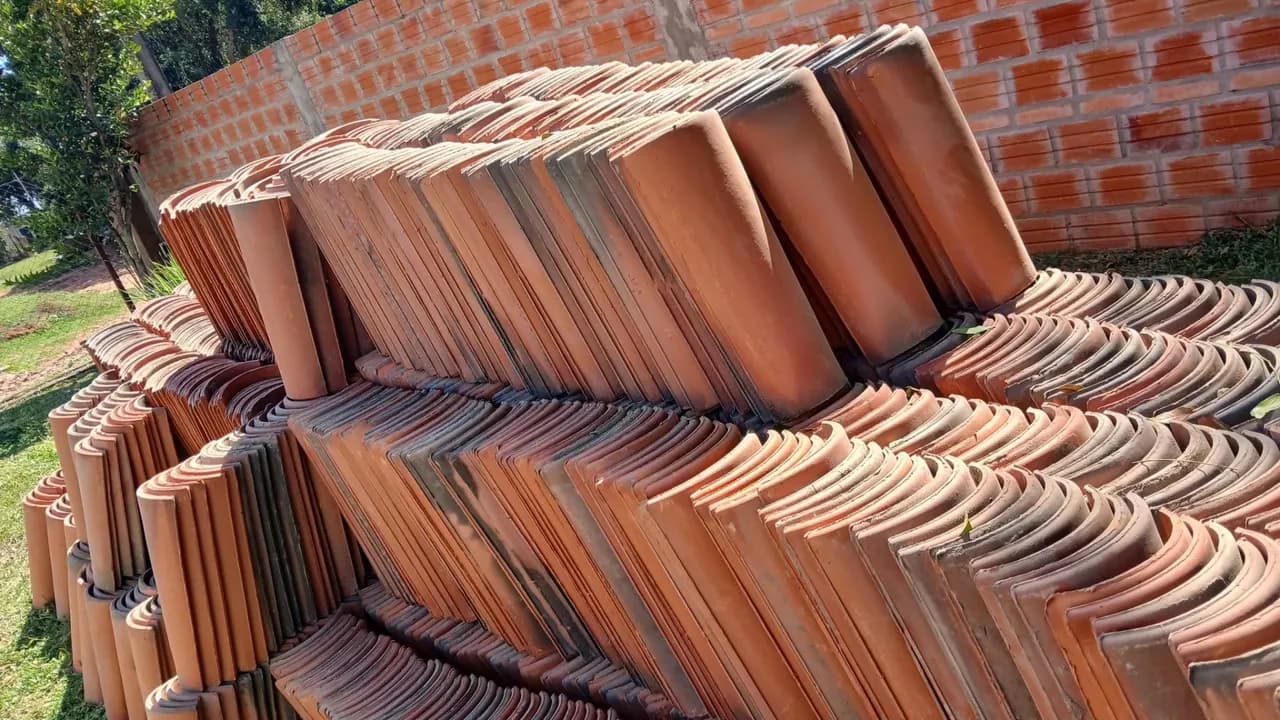 Pilas de tejas cerámicas coloniales apiladas al aire libre junto a una pared de ladrillos vistos.