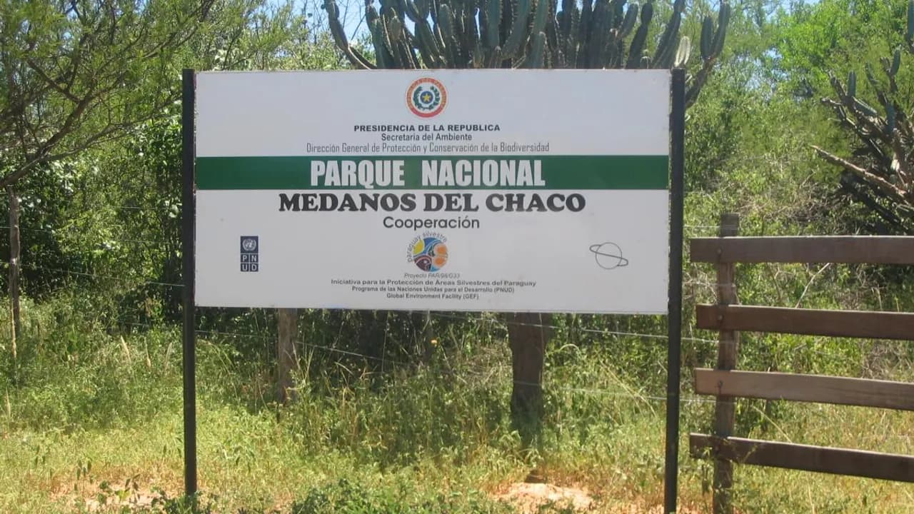 Cartel informativo del Parque Nacional Médanos del Chaco ubicado junto a un alambrado y vegetación silvestre