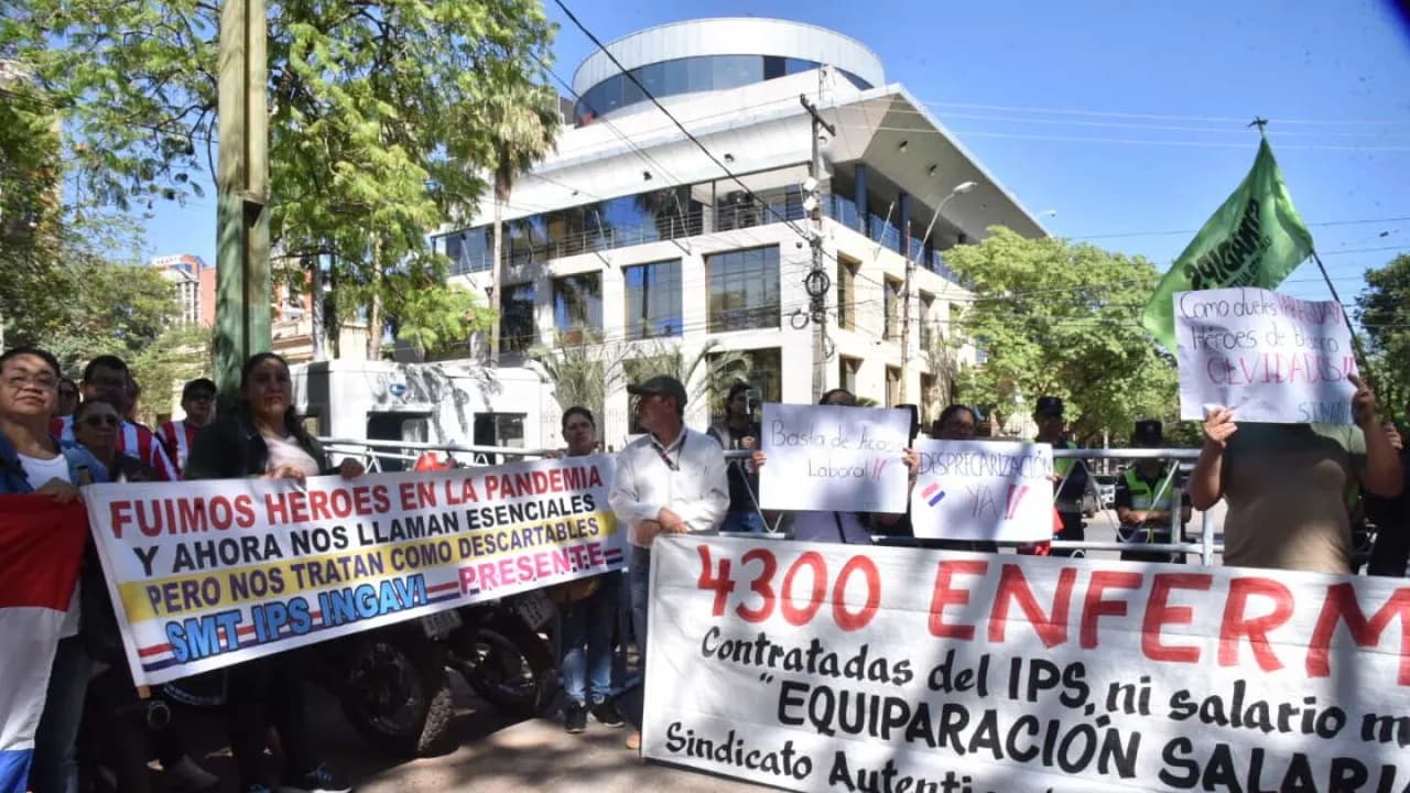 Un grupo de manifestantes sostiene pancartas con reclamos laborales y salariales frente a un edificio urbano moderno.