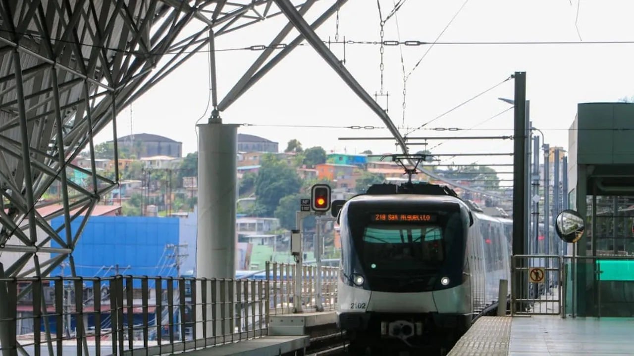 Tren moderno del Metro de Panamá aproximándose a una estación techada con estructura metálica y semáforo en rojo.