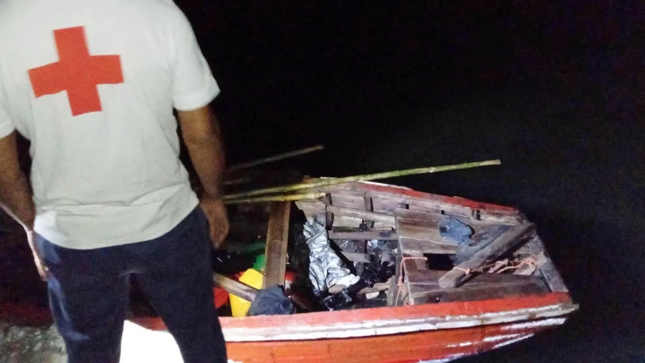 Socorrista de la Cruz Roja junto a una pequeña barca de madera precaria y reforzada con cañas.