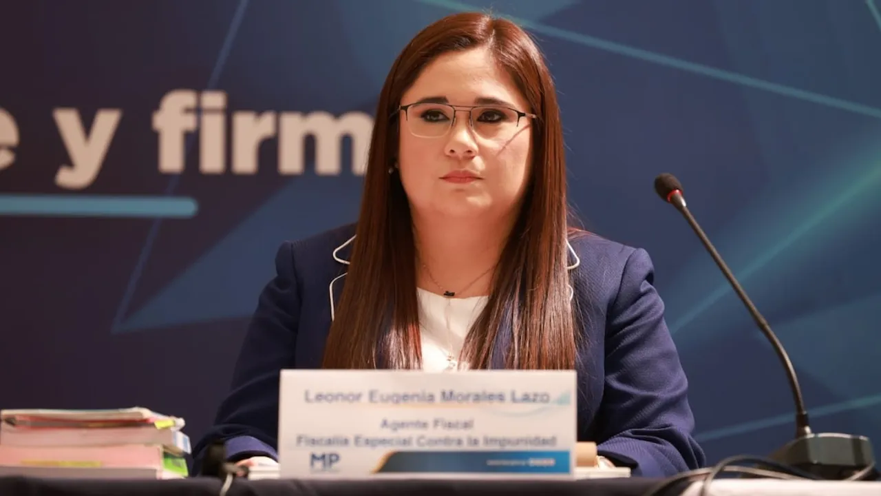 Leonor Morales Lazo sentada en una mesa de conferencia con un micrófono y su identificación oficial frente a ella.