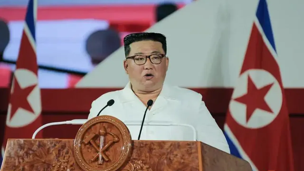 Kim Jong Un habla frente a micrófonos en un atril de madera con banderas norcoreanas de fondo durante un acto oficial.