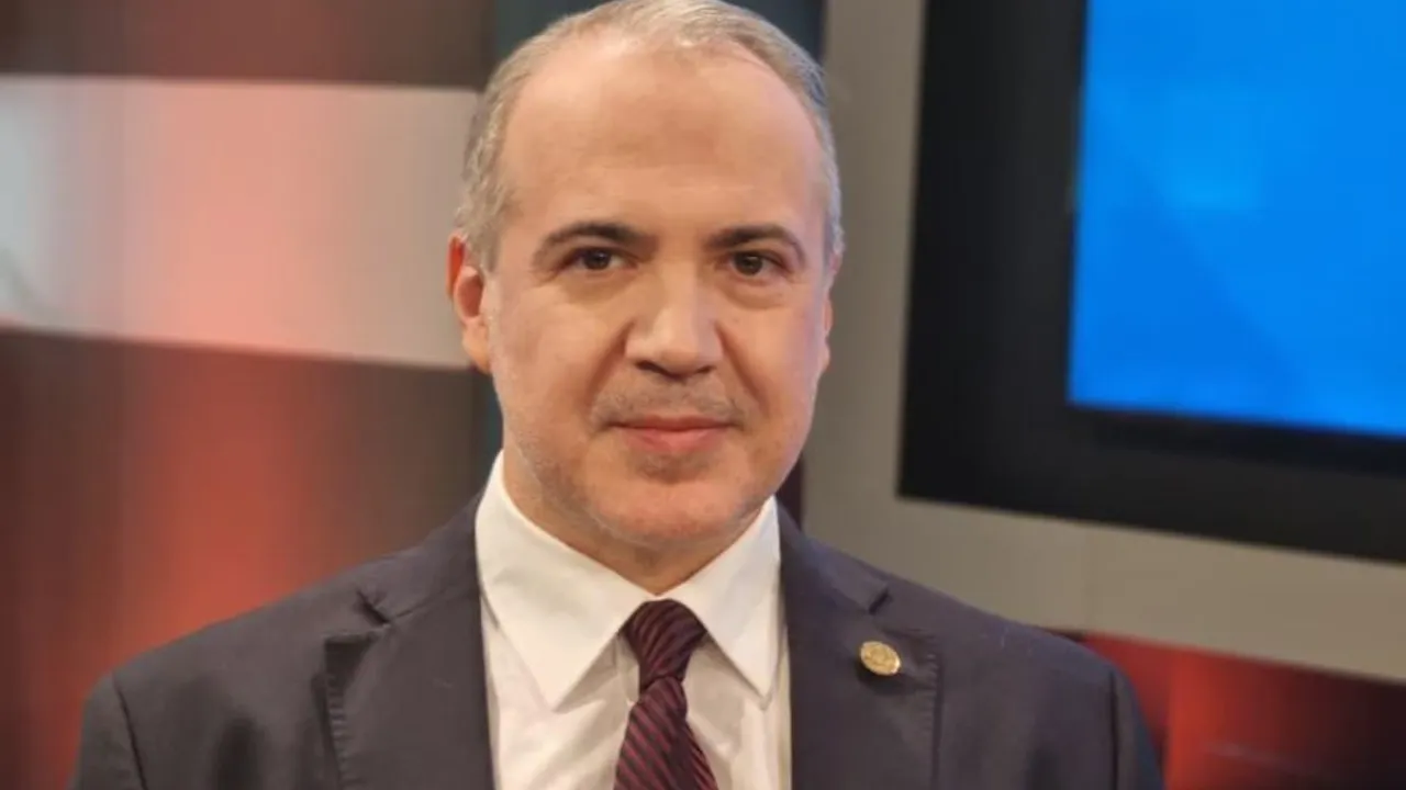 Fernando Beconi, con traje oscuro, camisa blanca y corbata, posa sonriente frente a cámaras en un set.
