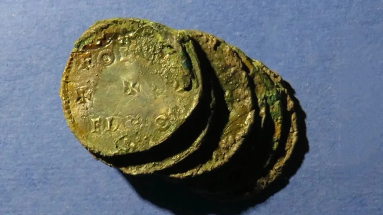 Pequeño grupo de monedas antiguas de plata corroídas y adheridas entre sí sobre una superficie azul.