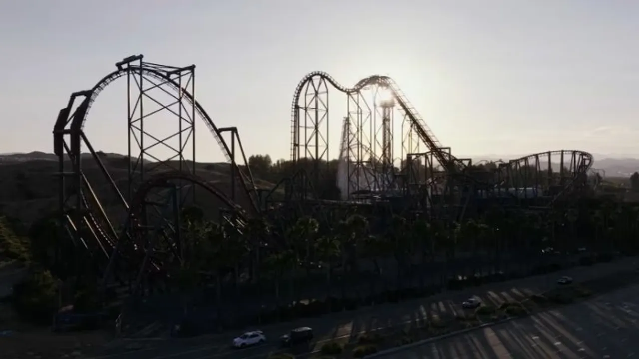 Estructura metálica de una imponente montaña rusa recortada a contraluz frente al sol durante el atardecer