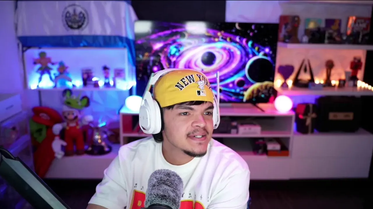 Joven con auriculares blancos y gorra amarilla frente a un micrófono en una habitación con luces decorativas.