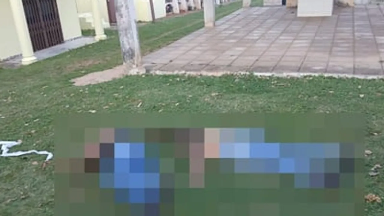 Cuerpo con censura sobre el césped frente a panteones y vereda de un cementerio.