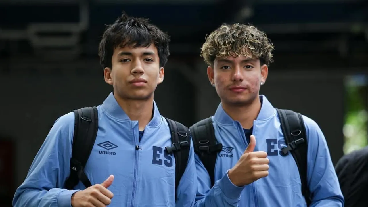 Dos jóvenes futbolistas con chaquetas deportivas celestes sonríen frente a la cámara y uno de ellos levanta el pulgar.