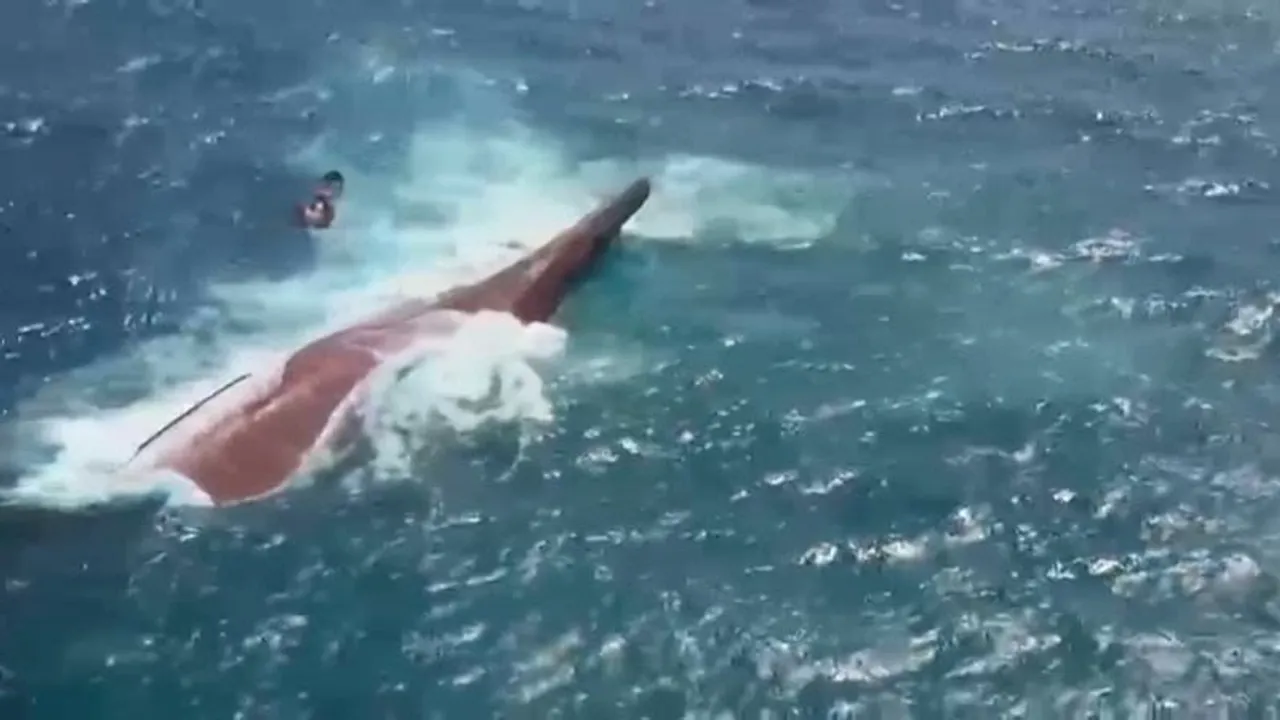 Casco de una embarcación volcada en aguas agitadas mientras olas rompen contra la estructura en el mar.