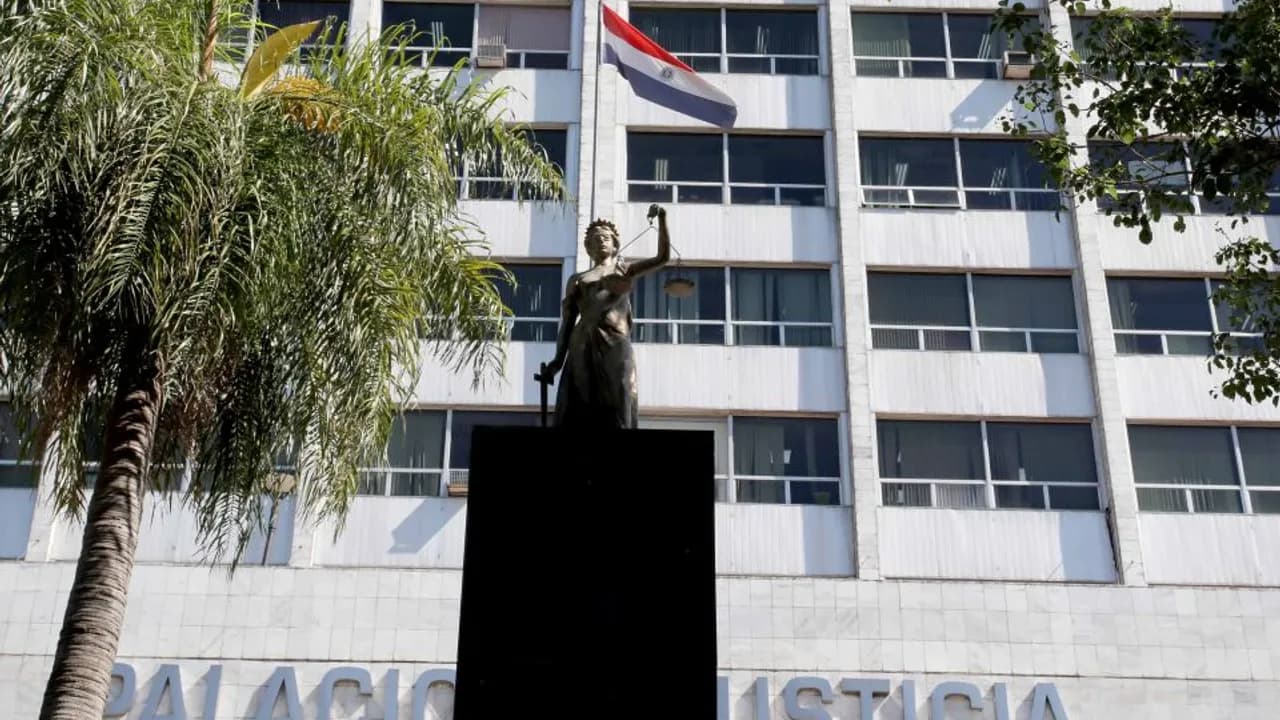 Estatua de la Justicia frente a la fachada del Palacio de Justicia con la bandera paraguaya de fondo