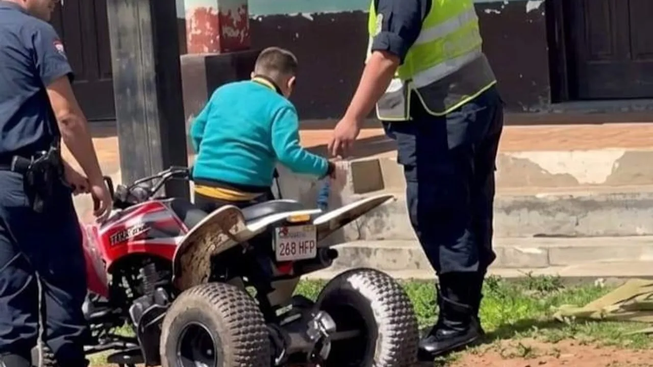 Efectivos policiales retienen a un niño sobre un cuatriciclo rojo estacionado junto a la vereda de una comisaría