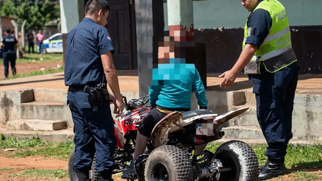Agentes de la Policía conversan con un niño con rostro pixelado sentado sobre un cuatriciclo rojo en la vía pública.