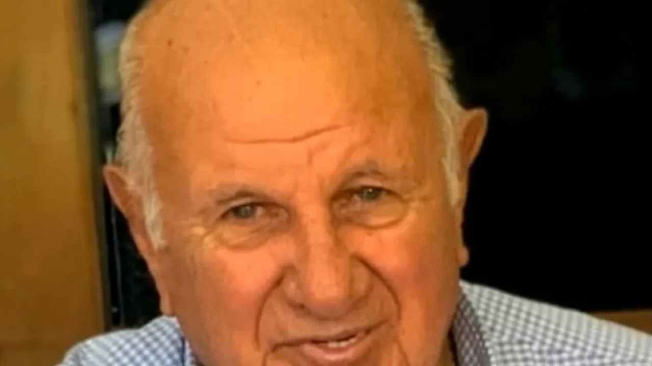 Primer plano de Óscar Denis sonriendo con camisa a cuadros y fondo oscuro en una reunión