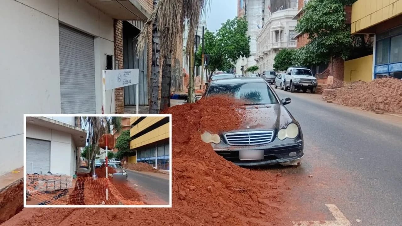 Automóvil negro cubierto parcialmente por un montículo de tierra roja en una calle céntrica.
