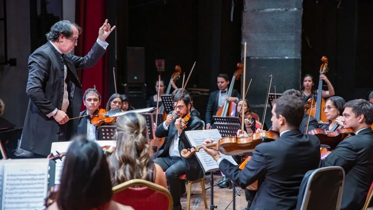 El director de orquesta marca el compás ante músicos de violín y contrabajo sobre el escenario.