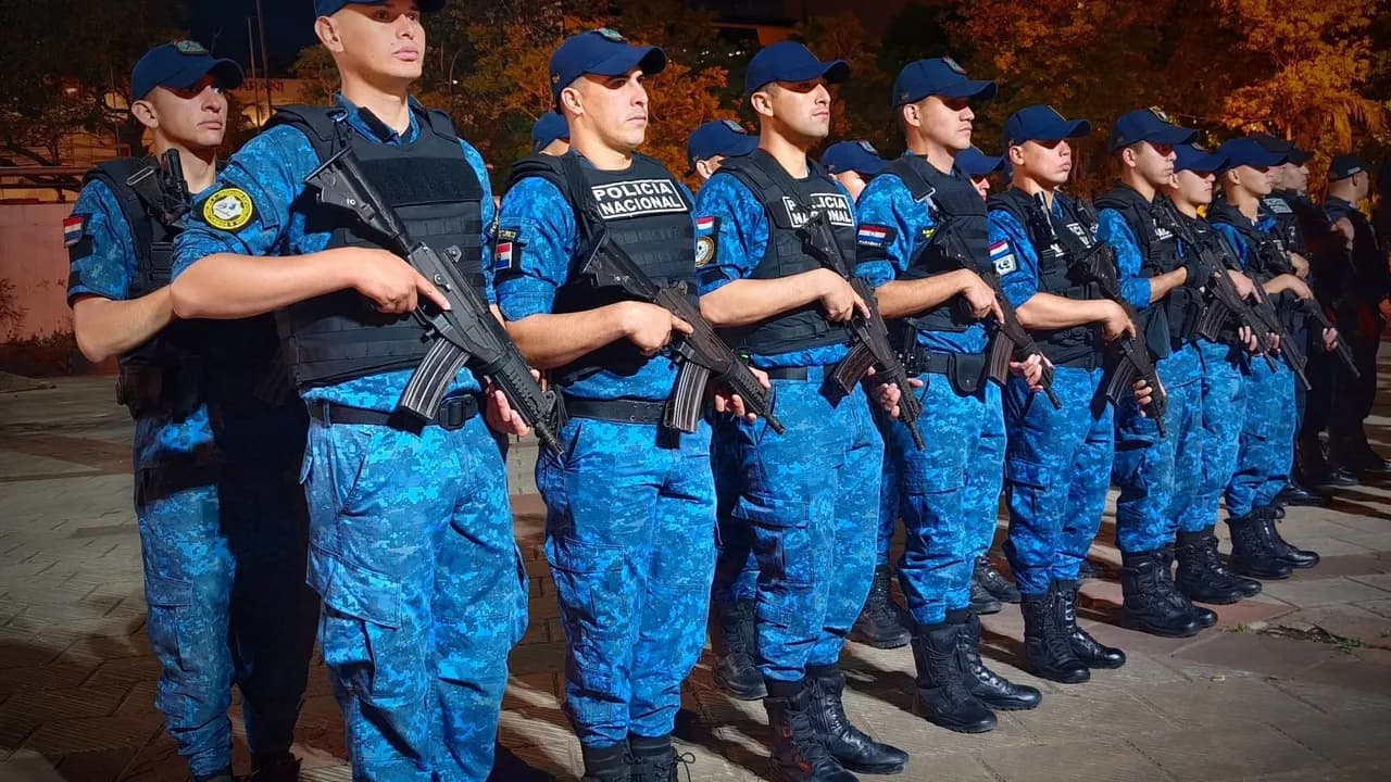 Agentes policiales de uniforme táctico camuflado azul y boinas sostienen armas largas formados en fila