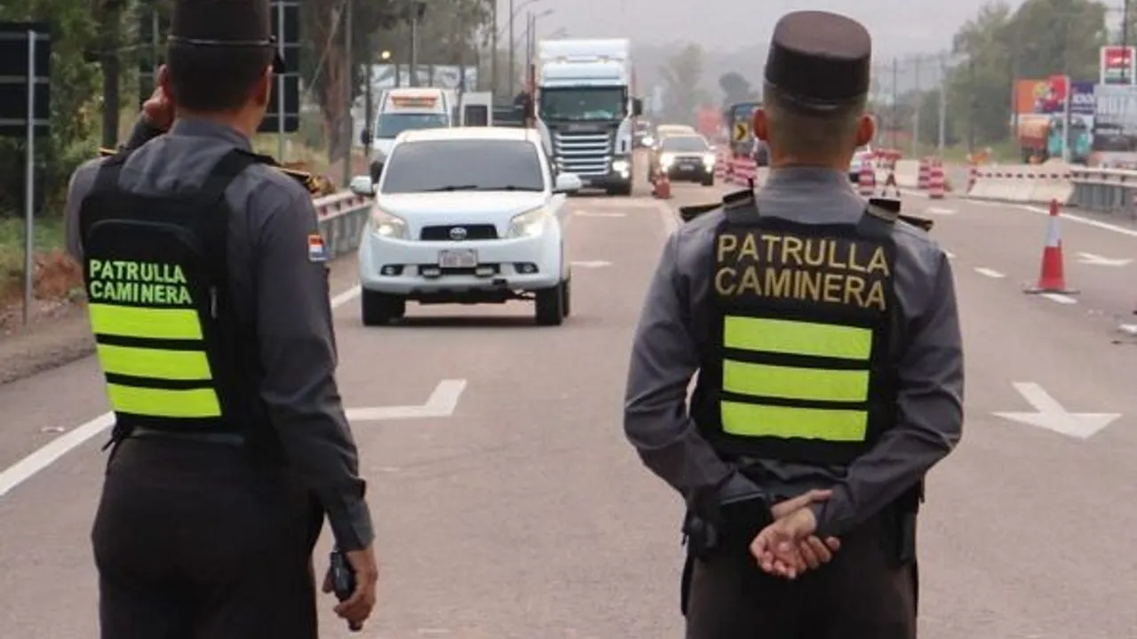 Agentes de la Patrulla Caminera de espaldas regulando el tránsito vehicular sobre una ruta asfaltada.