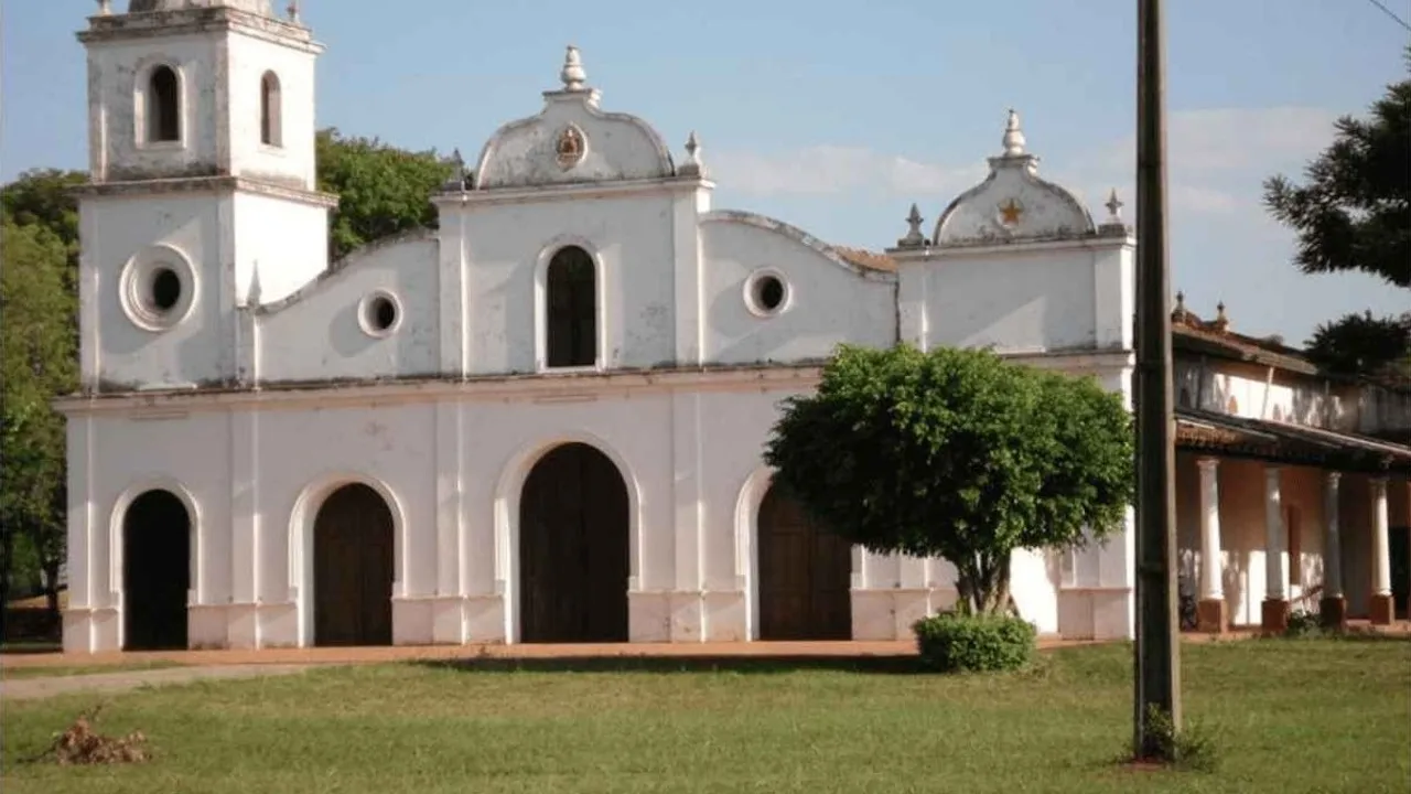 Fachada blanca de la histórica iglesia colonial de San Roque González de Santa Cruz rodeada de árboles y césped