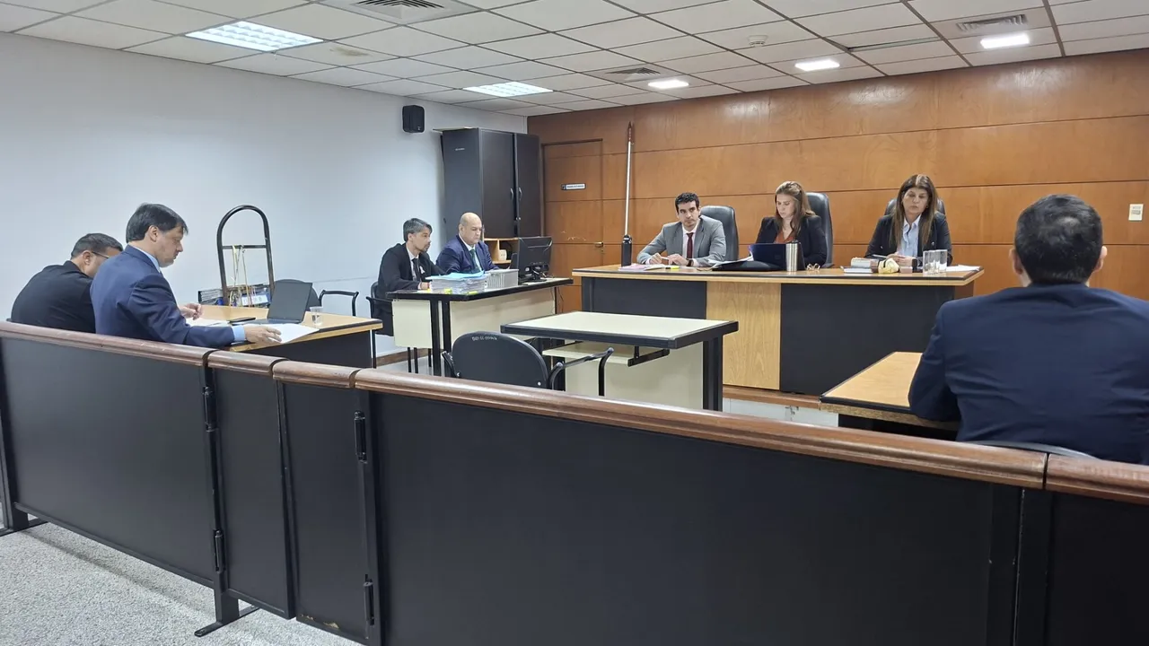 Tres jueces sentados en el estrado durante un juicio oral en una sala de audiencias con escritorios de madera.