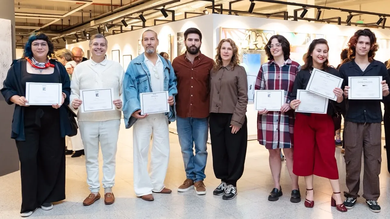 Grupo de artistas y organizadores posando en una sala de exposiciones mientras sostienen sus diplomas de premiación.