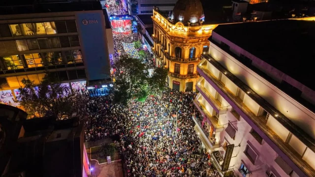 Multitud congregada de noche sobre una calle céntrica iluminada entre edificios históricos y modernos.