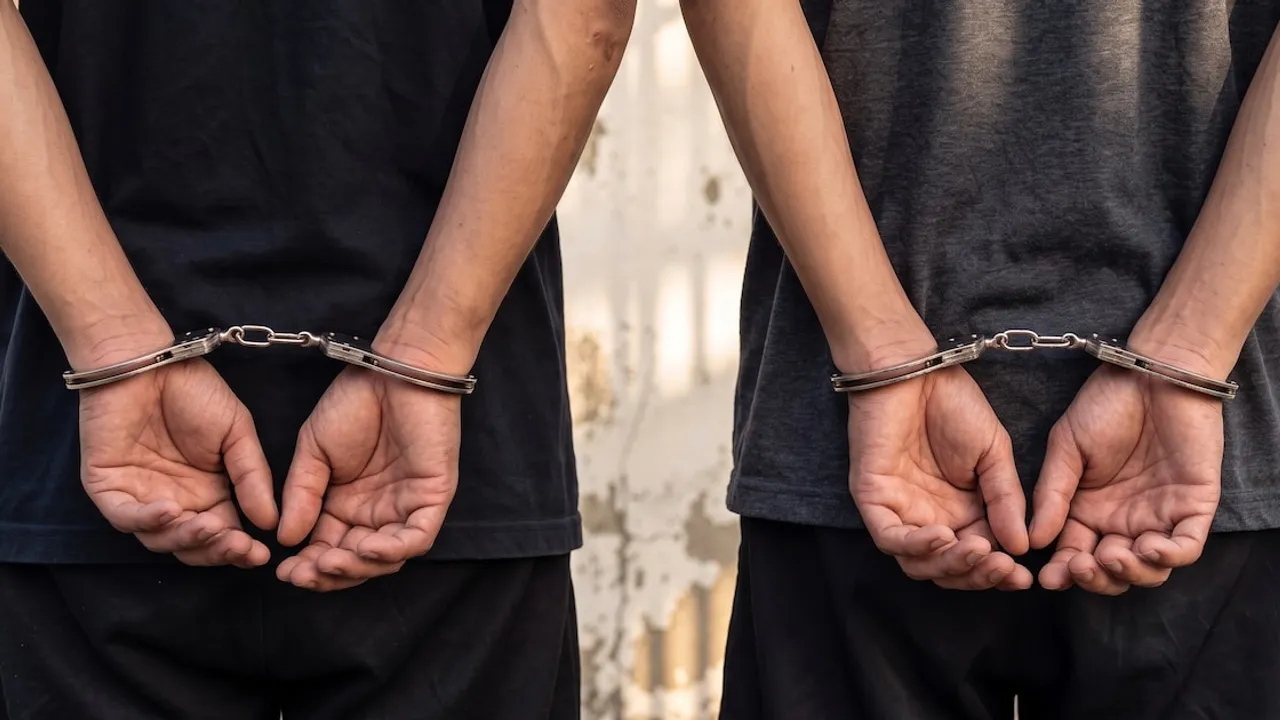 Dos personas de espaldas con remeras oscuras tienen las manos esposadas por detrás durante un procedimiento policial.