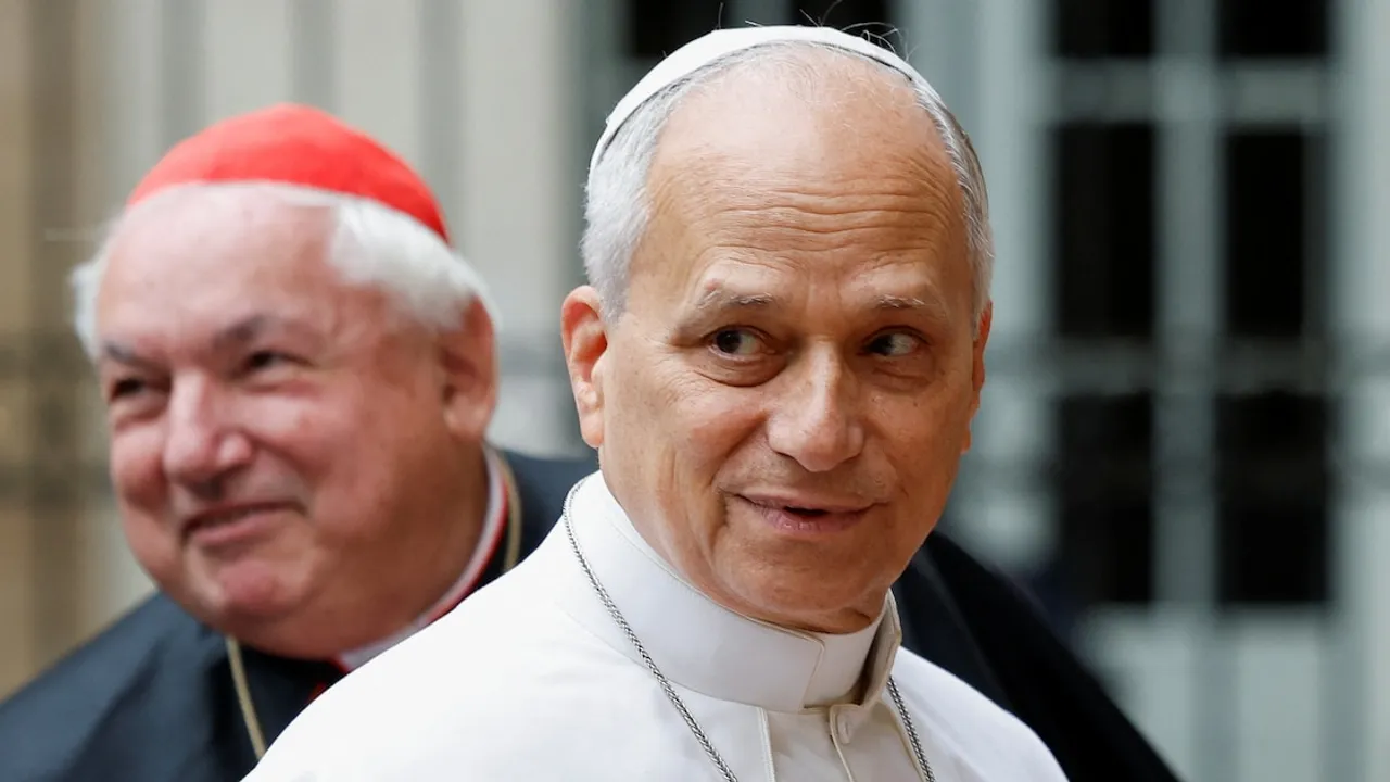 El papa León XIV con sotana blanca sonríe mientras un cardenal con solideo rojo lo acompaña en un acto público.
