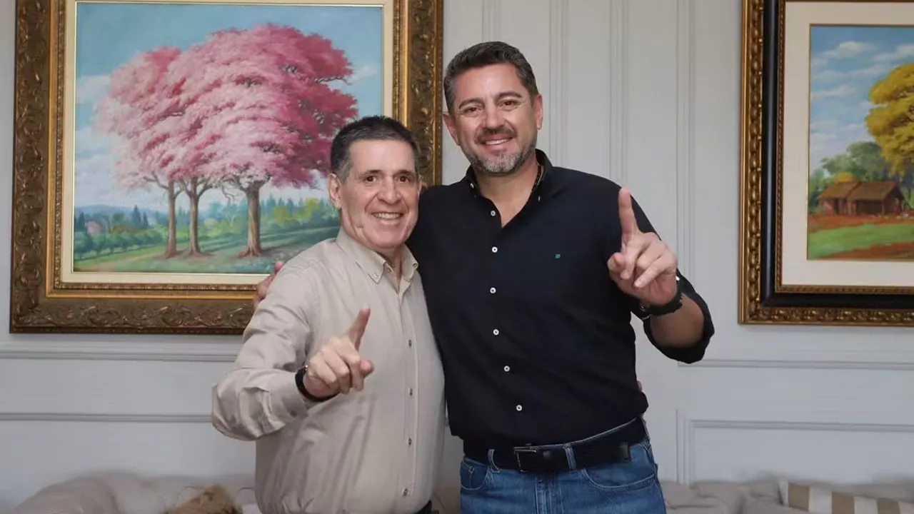 Horacio Cartes y Pedro Alliana sonríen juntos y señalan hacia arriba en una sala decorada con cuadros al óleo.