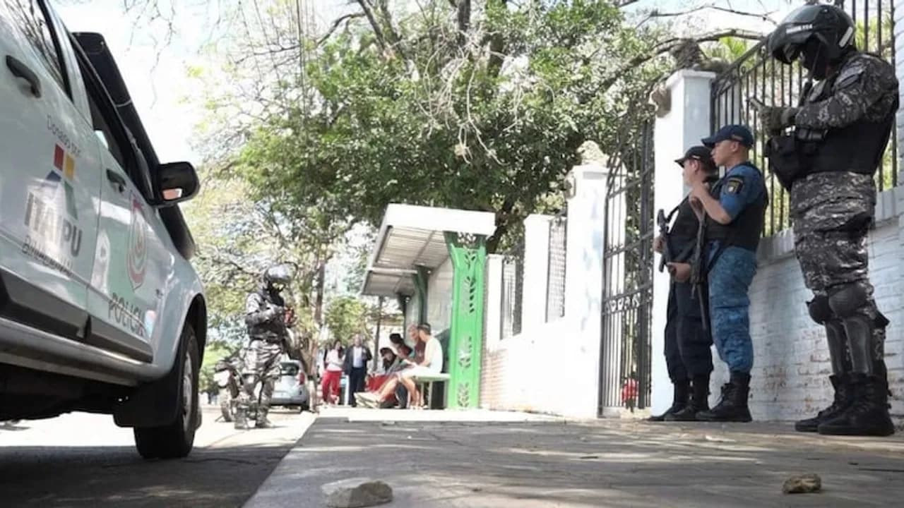 Agentes policiales y miembros del Grupo Lince custodiando la vereda frente al acceso de una institución educativa.