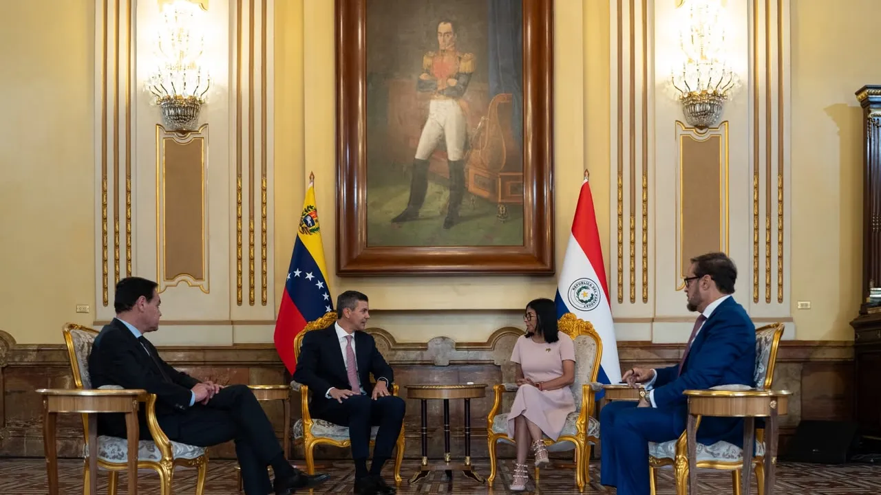 Cuatro autoridades dialogan sentadas en un salón formal con banderas de Paraguay y Venezuela bajo un cuadro histórico.