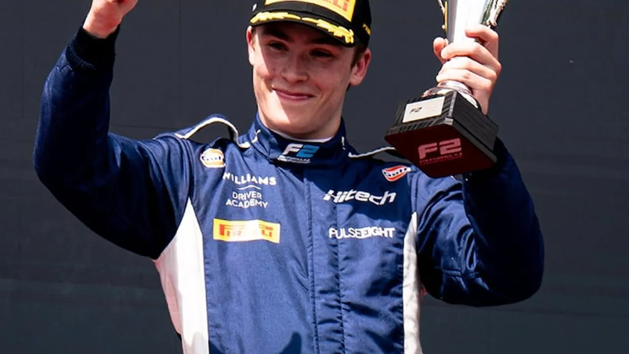 Luke Browning con buzo deportivo azul de piloto sonríe y levanta un trofeo con su mano izquierda