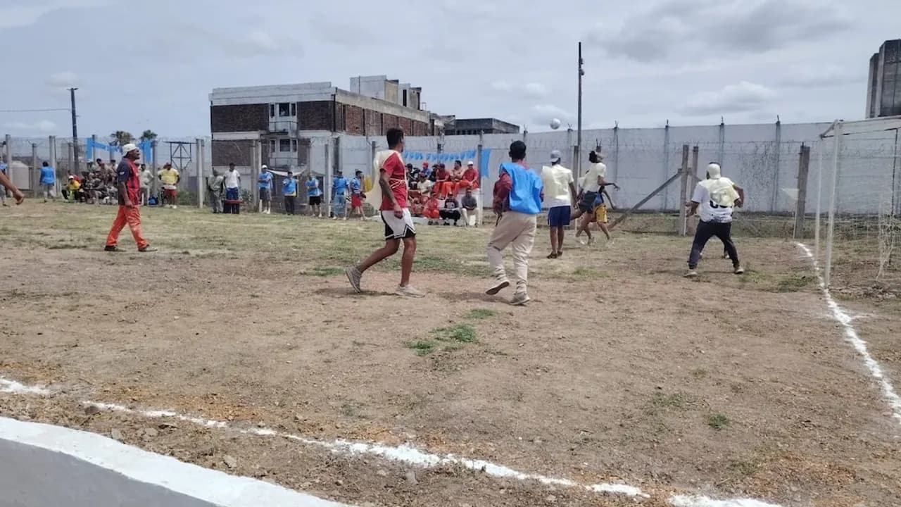 Personas privadas de libertad disputan un partido de fútbol en un campo de tierra dentro de un penal uruguayo.
