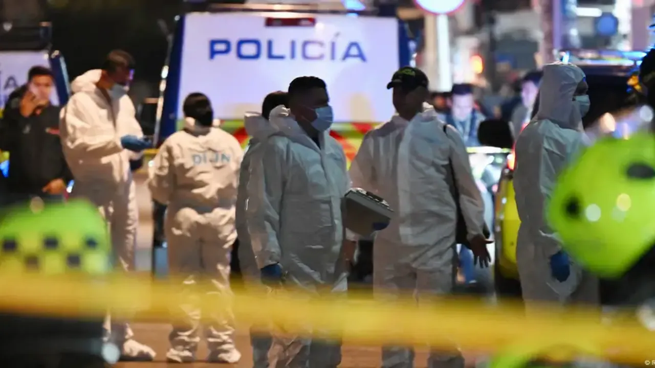Agentes policiales y peritos con trajes de protección blancos trabajan acordonando una calle durante la noche