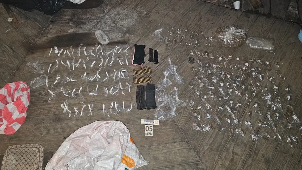 Dosis de presuntas drogas fraccionadas, proyectiles y cargadores sobre piso de madera durante un allanamiento judicial.