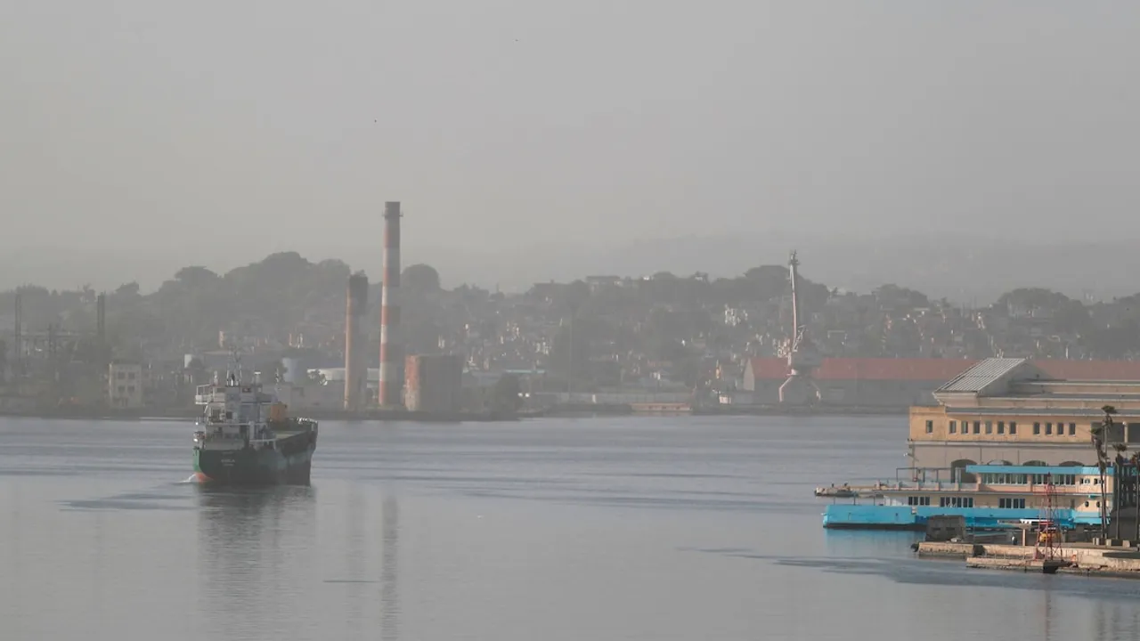 Barco de carga navegando en una bahía portuaria bajo una densa capa de bruma y cielo opaco