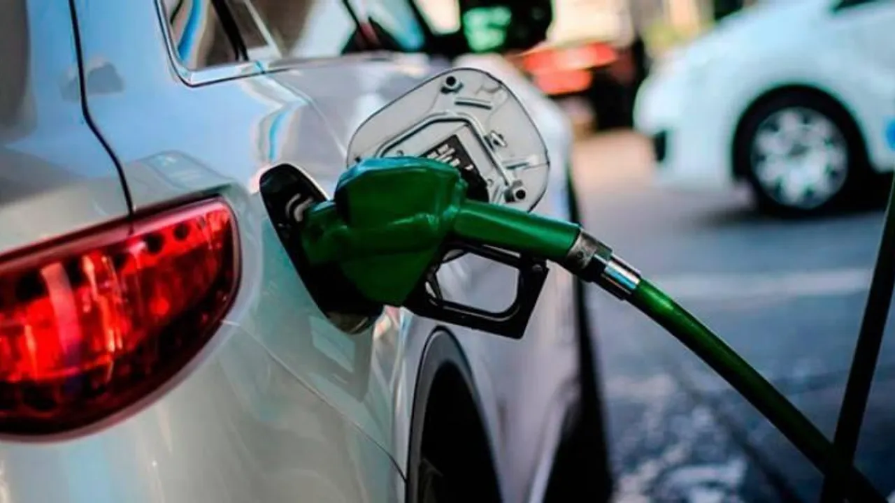 Pico verde de un surtidor de combustible cargando carburante en el tanque de un automóvil blanco.