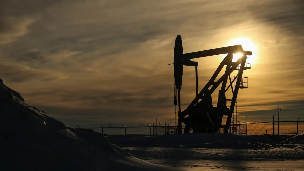 Silueta de una torre de bombeo petrolero al atardecer con el sol resplandeciendo detrás de la estructura metálica.