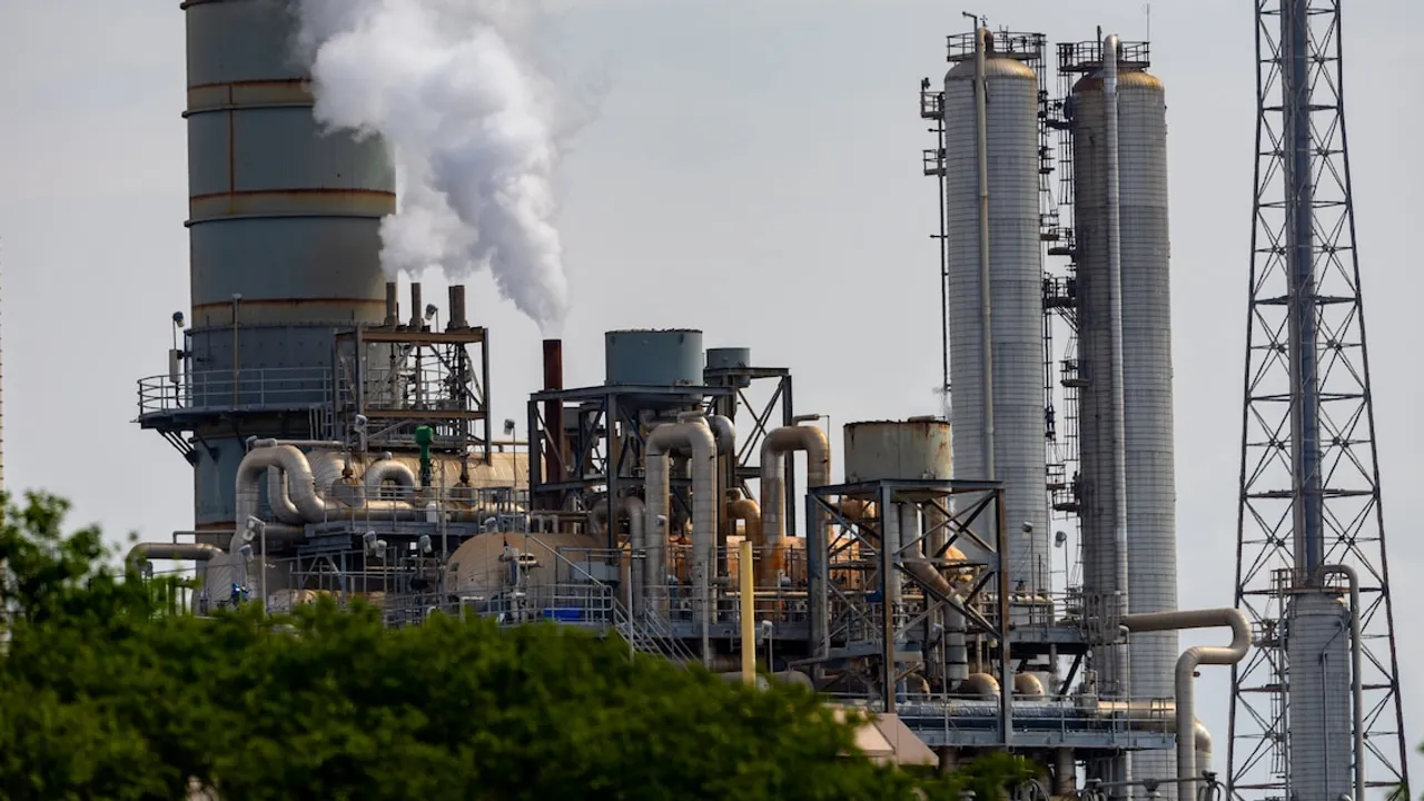 Instalaciones industriales con chimeneas metálicas, tuberías expuestas y emisión de vapor blanco bajo un cielo diáfano.