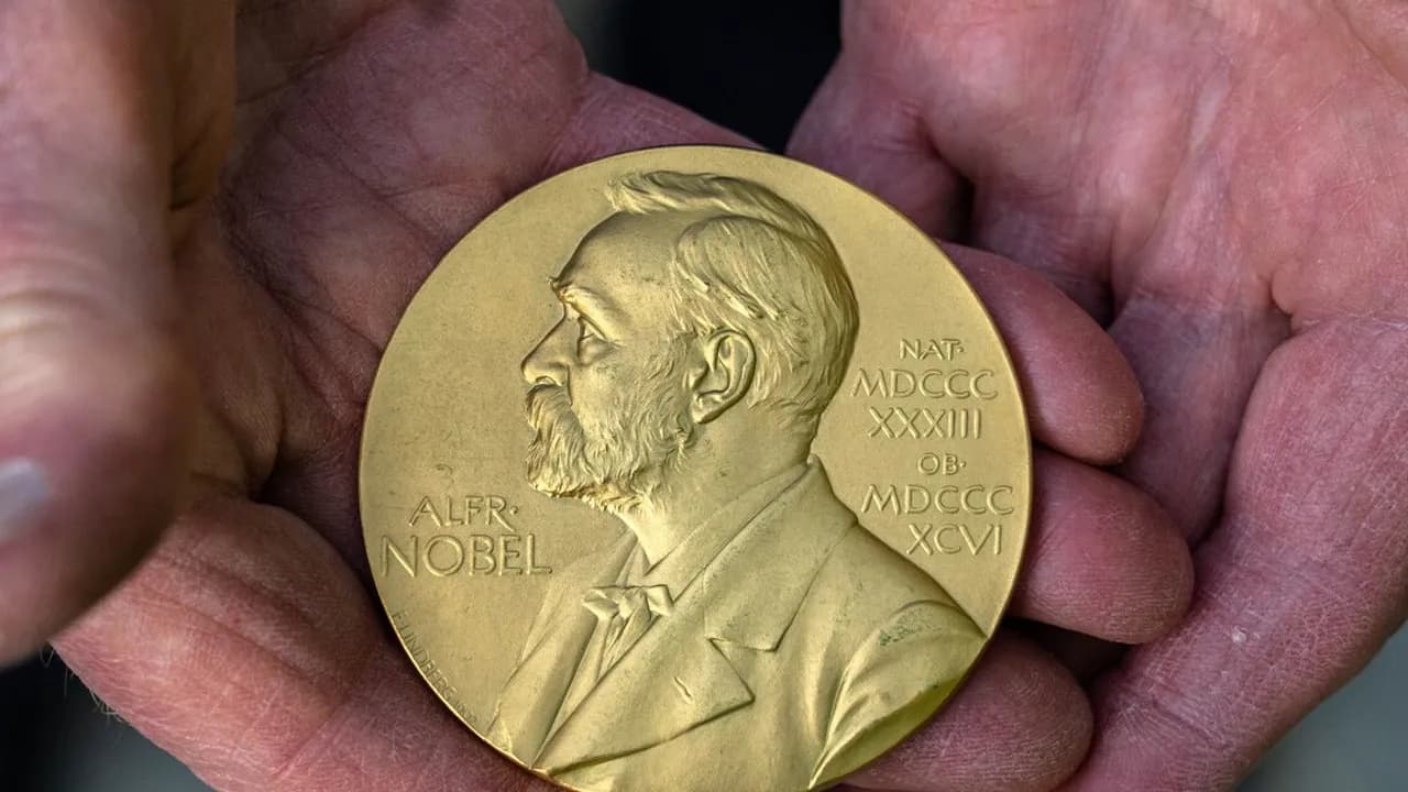 Manos sostienen la medalla dorada del Premio Nobel con el perfil grabado de Alfred Nobel y letras en relieve.