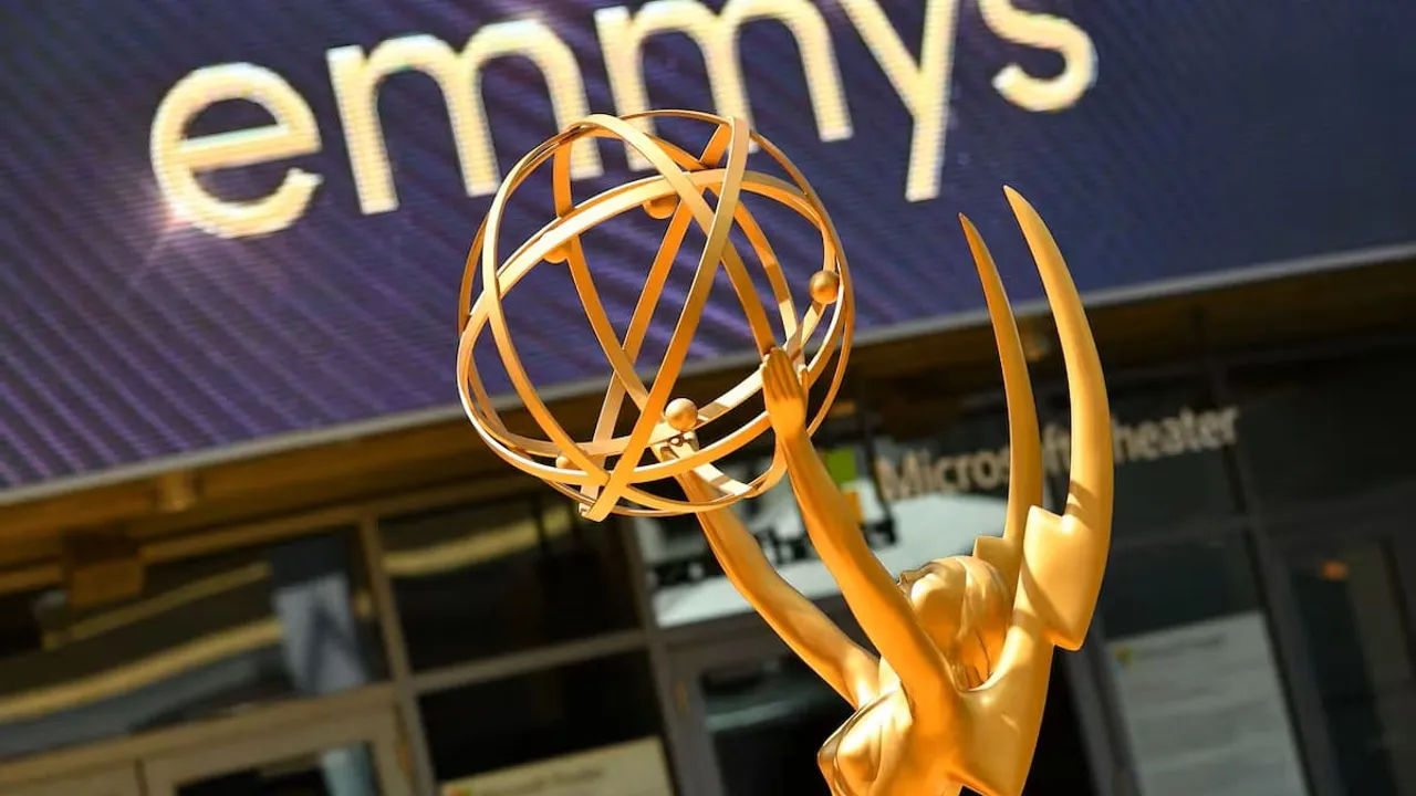 Estatua dorada de los premios Emmy en primer plano con el logotipo iluminado de fondo en una fachada exterior