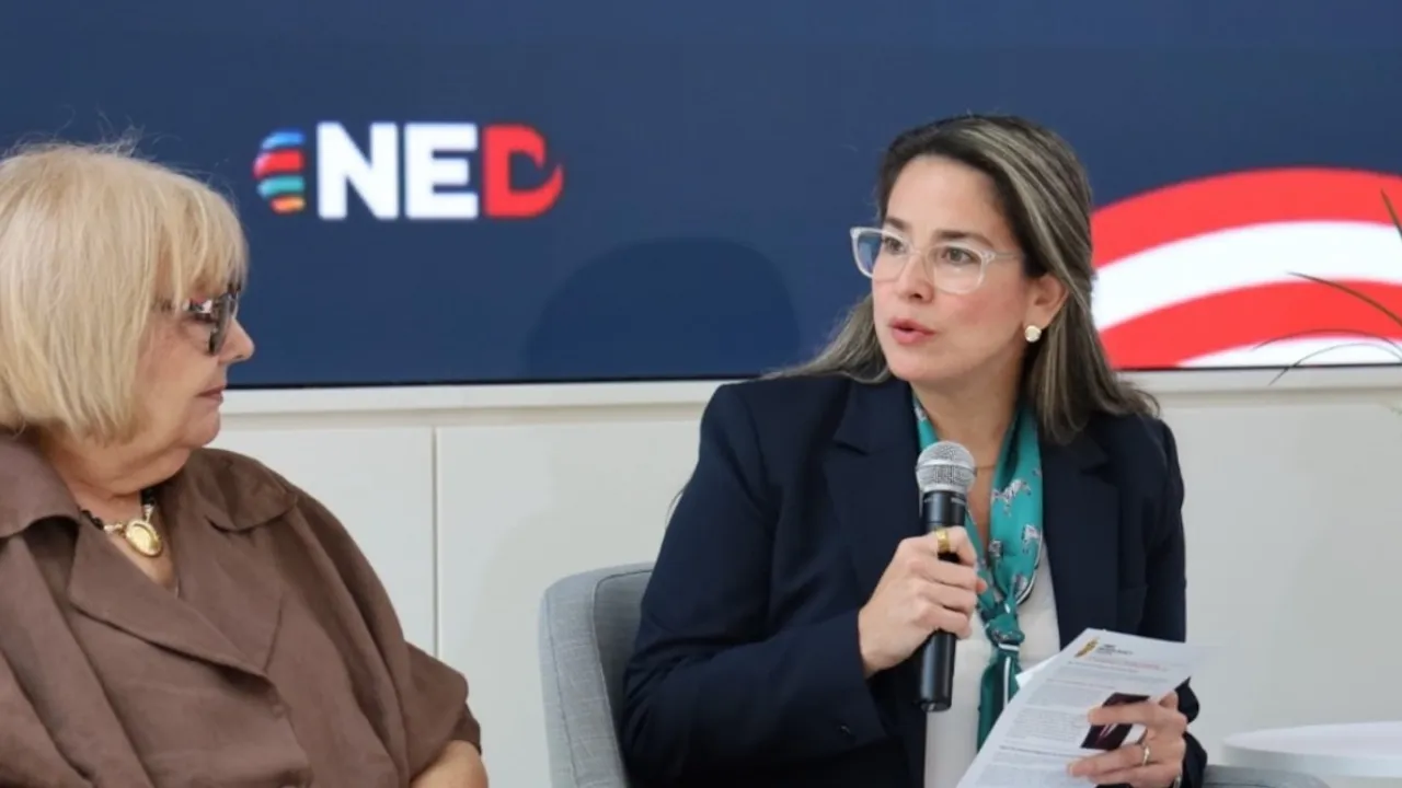 Berta Valle sentada con micrófono en mano durante una conferencia junto al logotipo de la organización NED.